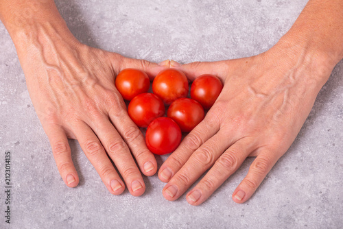 Hands with freshly harvested tomatoes on the table. Womans hands and cherry tomatoes, closeup with selective focus
