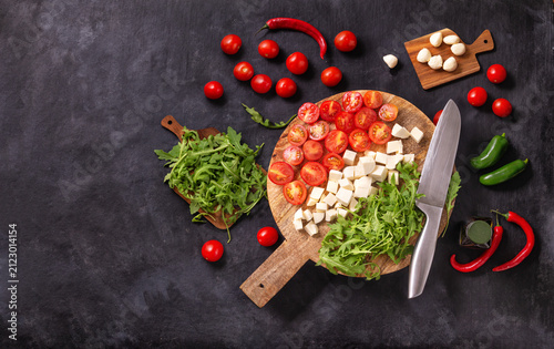 Top view of salad ingredients with mozzarella cheese, tomatoes and herbs on a wooden chopping board, flat lay, horizontal banner with space for text