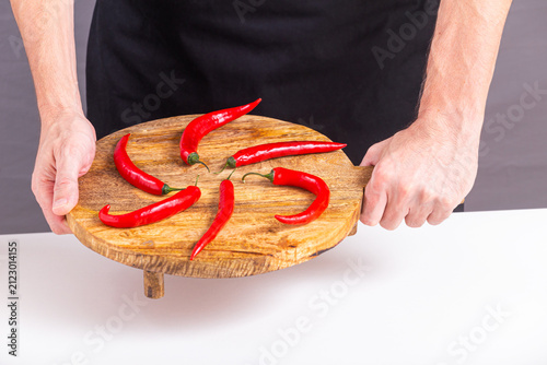 Close-up view of red chili peppers laid out on a cutting board in the hands of a male cook, selective focus