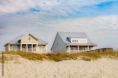 Canvas Print Two beach houses nestled in dunes under a cloudy blue sky