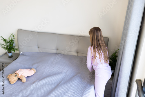 Konstfotografi Young girl in pajamas making her bed in a bright bedroom