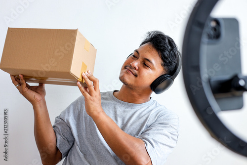 Asian Vlogger with Headphones Holding Parcel for Unboxing on Camera