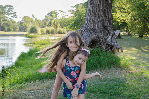 Two girls laugh beside a large tree by a calm lake
