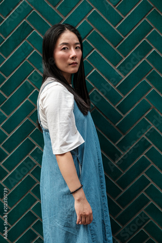Canvas Print Asian woman posing in denim overall against green tiled wall
