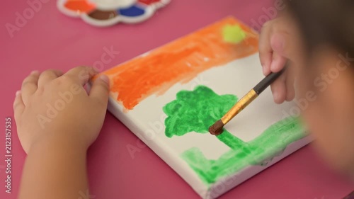 Child Painting Art: A young child's hands, holding a paintbrush, are actively engaged in painting a colorful landscape on a canvas, showcasing creativity and artistic expression.