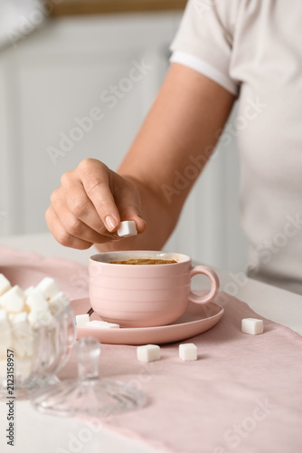 фотографія Womans hand adding a white sugar cube to a pink cup of coffee on a light pink ta