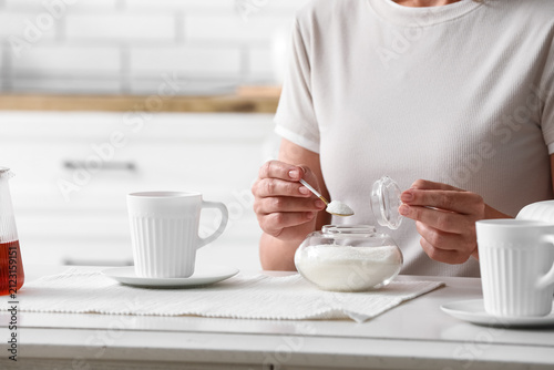 фотографія Woman adding sugar to a drink in a modern kitchen, sweetening beverages and heal