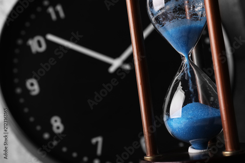 Konstfotografi Blue sand flowing in an hourglass with a blurred clock face in the background, t