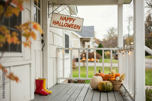 Happy Halloween sign hanging on a cozy front porch, autumn house entrance with pumpkins and string lights, seasonal fall home exterior decor