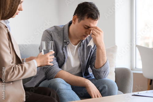 Male drug addict receiving glass of water from psychologist in office