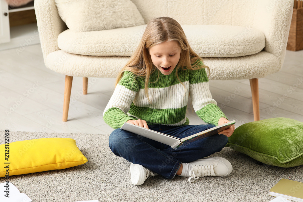 Fototapeta premium Shocked little girl reading book on floor at home