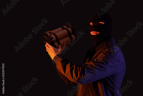 Handsome young man in balaclava with bomb on black background