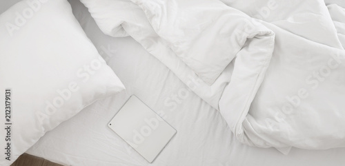 White tablet on unmade bed ...
