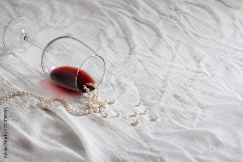 infidelity. Overturned red wine glass and scattered pearls on crumpled white tablecloth, scandal and infidelity concept, bar promotions.