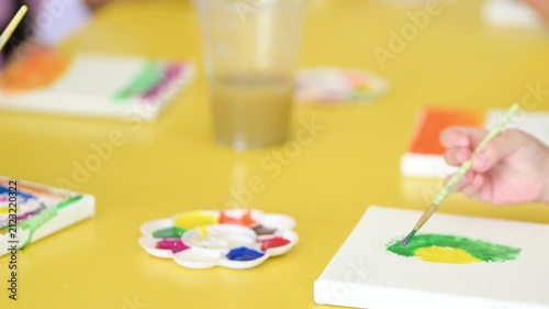 Close up of child’s hands in a painting class, creating colorful canvases with brushes and paints, encouraging artistic expression and group learning.
