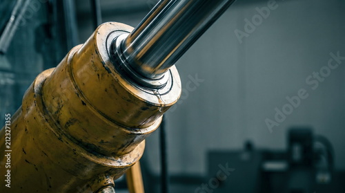 Hydraulic cylinder showing leaking fluid and wear in industrial workshop, highlighting heavy equipment maintenance and repair.