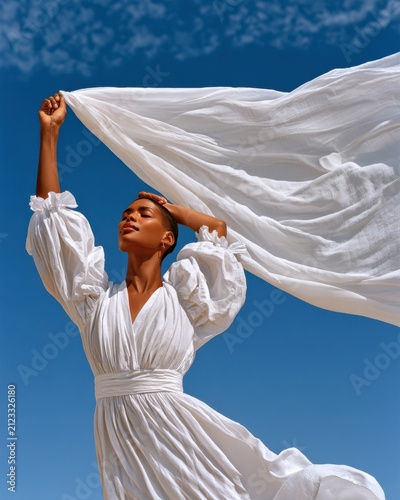 Woman in white dress with puffy sleeves holding flowing fabric against a bright blue sky