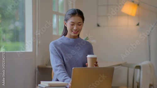 Work at home young asian woman working on laptop computer while sitting and hold coffee cup at home Morning lifestyle concept