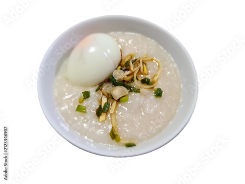 A bowl of Thai rice porridge with soft-boiled egg, fresh ginger strips, and sliced scallions, isolated on a clean white background, top view shot.
