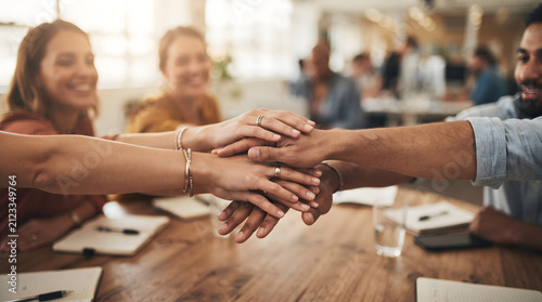 Happy diverse team building unity with hands stacked at wooden office desk together
