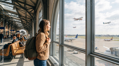 Beautiful woman with backpack at the airport window watching takeoff planes, aviation travel industry anticipation, symbolic journey of departure, freedom, and global adventure
