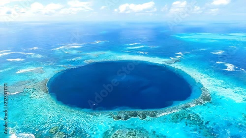 Aerial view of a deep blue ocean sinkhole with turquoise water and tropical island surroundings