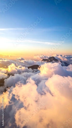 A serene aerial view of fluffy clouds illuminated by warm sunset hues against a clear blue sky