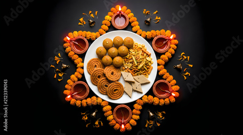 Top view of traditional diwali snacks and sweets arranged on a plate surrounded by glowing clay oil lamps