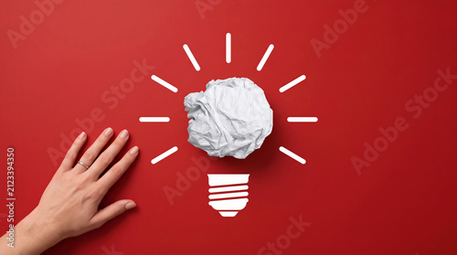 Hand reaching for a crumpled paper light bulb on a red background. Creative concept for innovation, brainstorming, and finding solutions