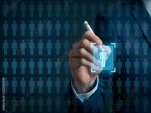 Businessman using a stylus to select a single human figure from a large grid of people on a digital interface for human resources