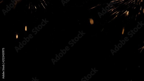 Abstract golden sparks overlay effect flying up and falling down in slow motion against a dark black background, ideal for compositing video footage and VFX.