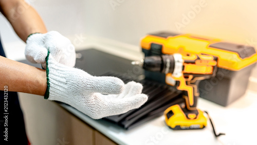 Male hand of maintenance worker putting on protective gloves near electric screwdriver and tool box in modern kitchen. Technician man preparing work tool for home appliance repair service