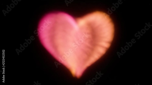 Abstract pink and orange glowing heart shape on black background. Soft bokeh light effect overlay symbolizing love, romance, passion, and Valentine's Day.
