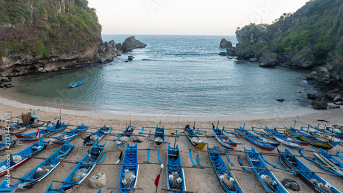 Colorful fishing boats line the sandy shore of a protected turquoise bay at Ngerenean Beach in Indonesia.