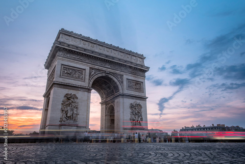 The Arc de Triomphe at twilight in Paris, France, with a colorful sunset sky and long exposure car light trails streaking past the historic monument