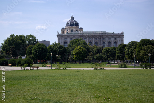 Facciata monumentale del Museo di Storia Naturale di Vienna sormontato dalla sua cupola, visto dall'ampio prato verde e dagli alberi del parco pubblico Volksgarten, Austria.