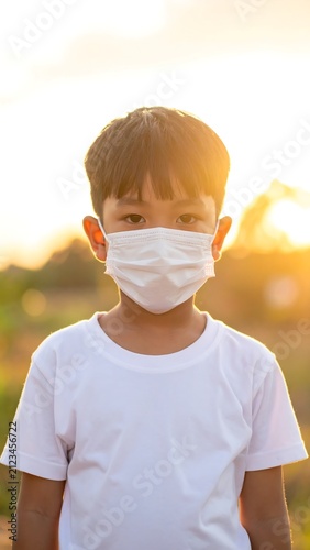 Young child in a face mask standing outdoors, backlit by sun