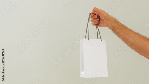 Картината върху платно Hand is holding a white shopping bag in a simple setting with plain wall behind
