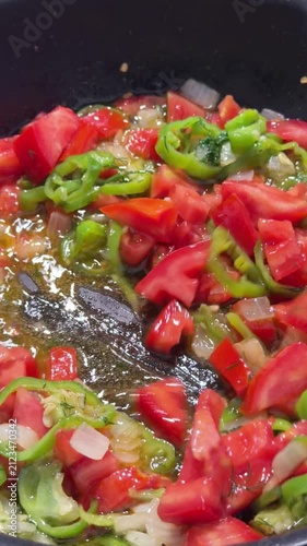 Close-up of fresh colorful vegetables being sauteed in a hot pan, featuring diced potatoes, carrots, green peppers, and red chili peppers being stirred with a spatula. Perfect for cooking tutorials, h