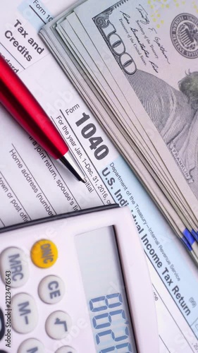 Close-up of US tax form, calculator, pen and one hundred dollar bills for finance and accounting concepts.