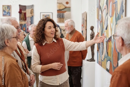 Museum guide explaining abstract painting to a group of elderly visitors in an art gallery