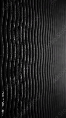 Black wavy ribbed texture slow pan. Close-up of deep black textured surface with vertical wavy ridges. Smooth linear camera movement reveals shifting light and shadow across the pattern.