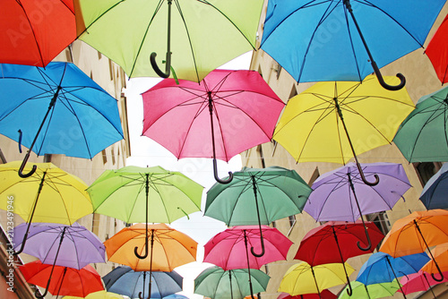Colorful umbrellas hanging over a narrow city street against buildings.