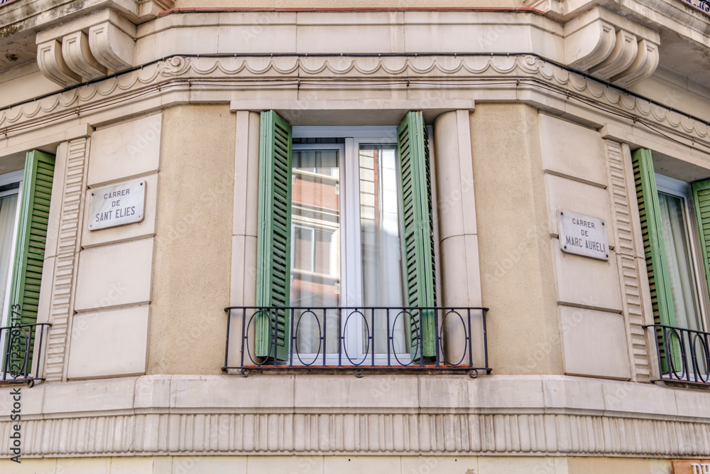 Obraz premium Traditional Barcelona Building Facade Corner with Green Shutters and Street Signs, Classic Architecture