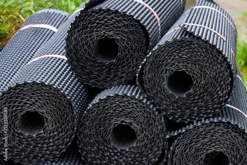 Canvas Print Stacked rolls of black dimpled HDPE drainage membrane stored at a construction site