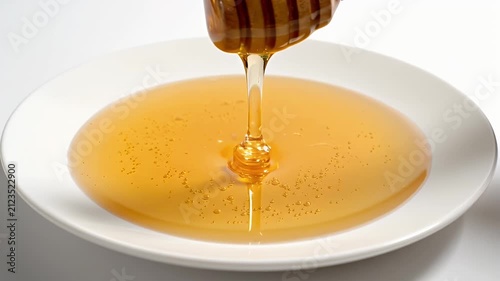 Golden Honey Dripping From Wooden Dipper Onto White Plate With Subtle Sparkles Isolated on White Background