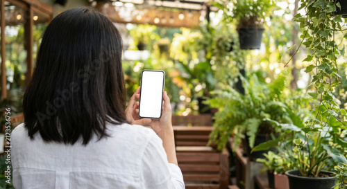 Woman holds smartphone with blank white screen mockup in cozy green garden