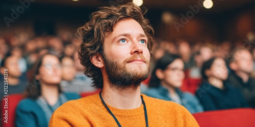 Adult Man Listening Attentively to Lecture in Crowded Auditorium with Blurred Audience Representing Professional Development and Educational