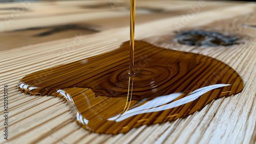Golden, Viscous Liquid Poured onto a Light Wood Surface with Pronounced Grain, Creating a Reflective, Irregularly Shaped Spill Spreading Across the Textured Board