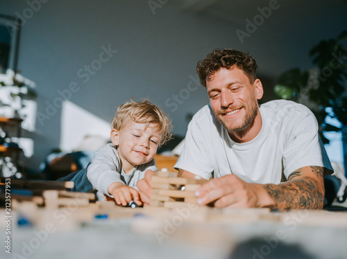 Happy Tattooed Father Laughing with Young Child at Home Dining Table